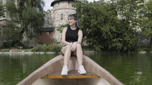 medium general shot girl black hair plaid skirt black t-shirt sitting in boat on green lake with castle vacation travel fun tourism amazing green water europe model