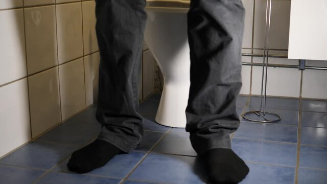 Man enters the bathroom and sits down on the toilet to relieve himself - knees and below static view