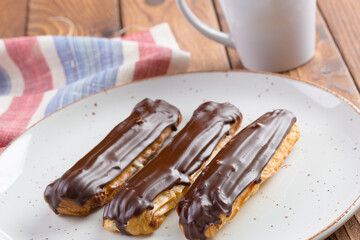 Chocolate eclairs on white plate on wooden table