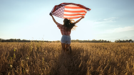 Young woman waves an american flag on the wheat field. Patriotic holiday, independence and freedom celebration. 4th of July concept.