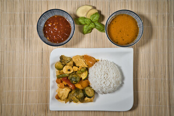 Eine Portion gelbes Reis Curry mit Hühnchen und frischem biop gemüse auf einem weißen Teller,...