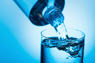 Pouring water from a bottle into glass on a blue background.