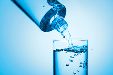 Pouring water from a bottle into glass on a blue background.
