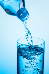 Pouring water from a bottle into glass on a blue background.