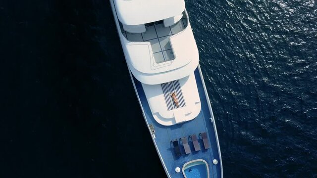 Drone top view on sensual sexy woman lay on deck of beautiful white boat. Private yacht cruise ticket lifestyle enjoying life in open sea. Rich and famous stars and celebrities