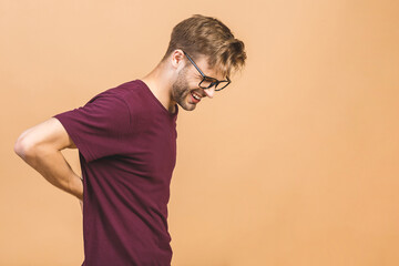 Young handsome man wearing casual t-shirt standing over isolated beige background. Suffering of backache, touching back with hand, muscular pain.