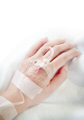 Close-up of saline solution in a patient's hand in clothing, lying on a hospital bed, the patient dripping saline on a white background.