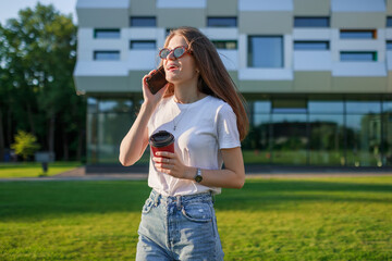 a student near the school in her free time talking on the phone holding a glass of coffee in her hands.