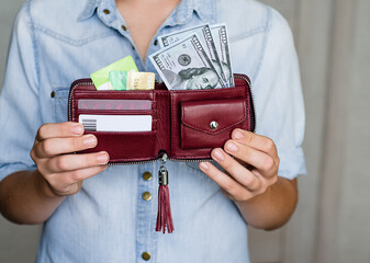 A dark red wallet with cash dollars and credit cards is held by a young man. Cash and non-cash...
