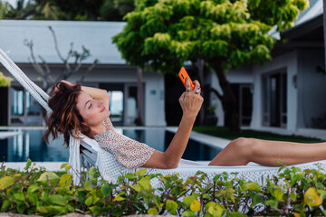 Woman with phone resting lying on hammock with mobile phone, take selfie, chat.  