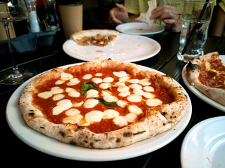 A large round pizza with cheese, tomatoes and herbs is on the table in an italian restaurant, blurred background