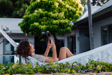 Woman with phone resting lying on hammock with mobile phone, take selfie, chat.  