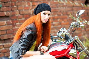 Naklejka na ściany i meble Portrait of charming young woman with red hair near a motorcycle