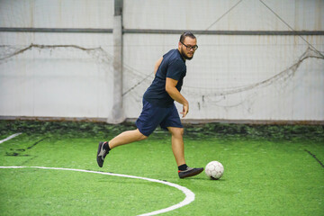 man playing football indoor on green lawn on soccer arena. Amateur sport