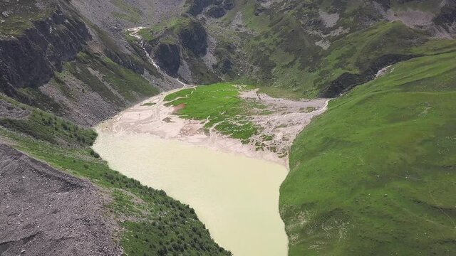 Top view of lake from meltwater in mountains. Clip. Amazing lake formed in mountain pass from melted water from glaciers. Muddy lake between green mountains
