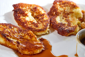 Pancakes on white plate and sweet liquid honey or caramel with a small spoon and with background. Delicious fried flour food. Unhealthy and harmful, but very tasty food.