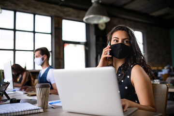 Portrait of young businesswoman with face mask working indoors in office.