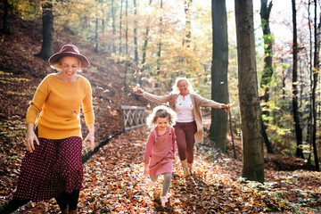 Small girl with mother and grandmother on a walk in autumn forest.