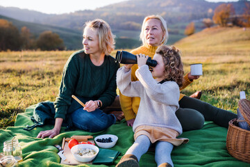 Small girl with mother and grandmother having picnic in nature, using binoculars.