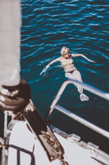 Young woman in bikini swimming around sailing boat yacht in deep blue sea ocean.