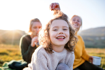Small girl with mother and grandmother having picnic in nature, having fun.