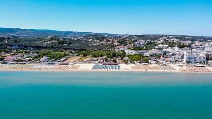 Fototapeta na wymiar Aerial view of the Spiaggia di Castello, south of Vieste on the Gargano Peninsula in Italy - Alignements of umbrellas in summer for holiday goers in the Adriatic Sea