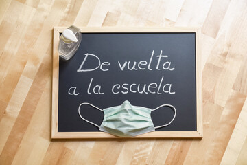 Blackboard with handwritten label "back to school", facial mask and dispenser of hydroalcoholic gel. Protective elements for returning to classrooms.