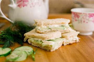Cucumber English Tea Sandwiches with Dill and Cucumber Surrounding it and a Pink and White Teapot in the Background.