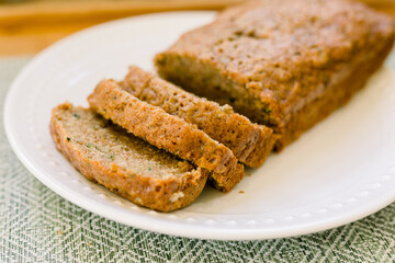 A loaf of zucchini bread, half of it sliced on a white plate.