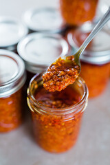 A vertical photo of a metal spoon with Thai Chili Paste / Chili Sauce (also called chili oil, or Naam Prik Phao) and Vietnamese Lemongrass Chili Garlic Sate ("tuong ot sa te") 