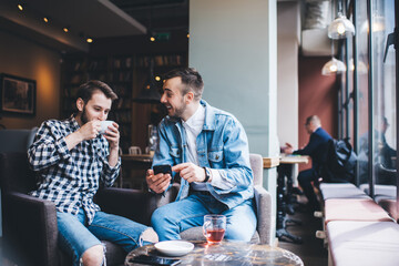 Fototapeta na wymiar Cheerful men using smartphone in modern cafe and laughing