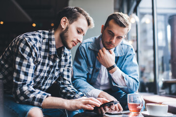 Two men resting in cafe surfing smartphone