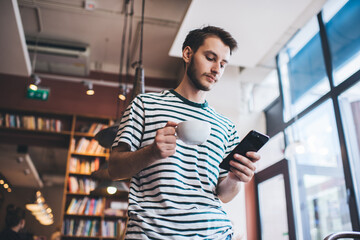 Man with drink using smartphone in library