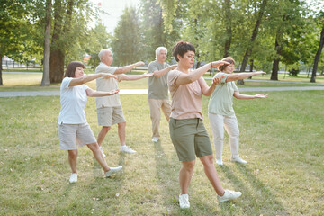 Group of focused senior people and their coach gesturing hands and doing qigong exercise in park - obrazy, fototapety, plakaty