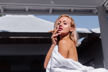 Fashion outdoor portrait of naked woman sit on sofa cover herself with blanket holding cigar, natural  day light.    