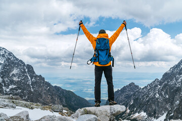 Dressed bright orange jacket backpacker man with raised armswith  trekking poles enjoying the...