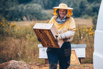 Portrait of a beekeeper in protective wear carrying hive frame.