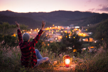 Young man feeling free and motivated at the top of a mountain with a lit kerosene lantern, watching...