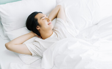 Top view of young Asian man smiling while sleeping in his bed and relaxing in the morning. Rest...