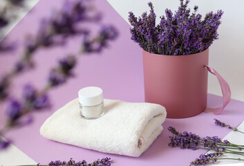 White bath towel with a jar of body cream on the background of a bouquet of blooming lavender, bokeh, lilac background, close - up-the concept of using aromatic plants in self-care