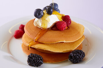Thick maple syrup pouring onto a stack of fresh pancakes. Selective focus.