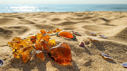 Obraz premium Baltic Amber jewelry vintage beautiful pendant, luxury necklace on the sand bathe in the sun. Idyll in the early morning on the beach.