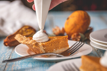 Hand using piping bag to garnish pumpkin pie with whipped cream