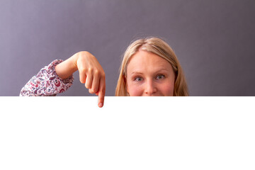 Junge Frau zeigt mit Finger auf weiße Fläche Hintergrund grau