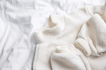 Warm fleece sweater on white crumpled fabric, top view