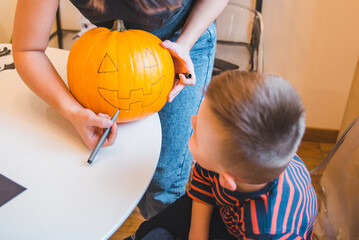 mother with son making pumpkin head at home together