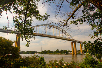 Wide angle image of the Chesapeake City Bridge that spans over the Chesapeake and Delaware canal (C and D canal) in the Back creek section of it. Image features the tall columns and the arched bridge.