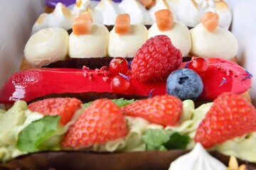 Tasty French eclairs with icing, cream, fresh berries and sugar decor elements. Set of delicious eclairs with creative colorful decor in white paper box. 
