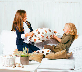 two cute sisters at home playing, little smiling girl in house interior on sofa, messing hair,...