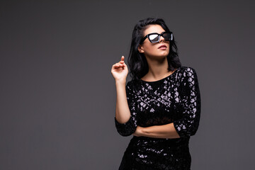 Portrait of a beautiful young woman in a fashionable dress and sunglasses posing on a gray background.